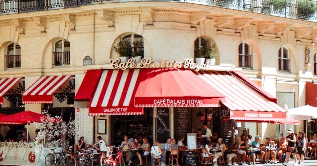 A bustling scene at Café Palais Royal in Paris with patrons enjoying a sunny day.